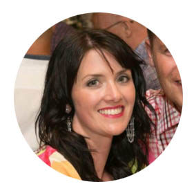 Smiling woman with dark hair wearing colorful clothing indoors.