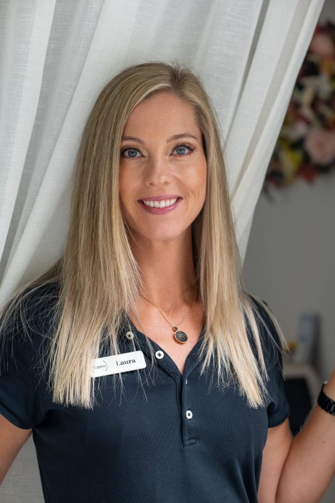 Smiling woman in a black shirt standing beside white curtains.